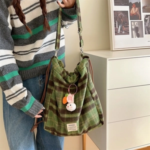 Detail of green and coffee plaid drawstring bucket bag with knitted rabbit charm and logo