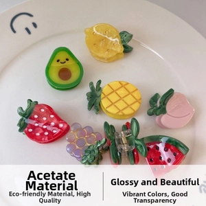 Macro view of assorted mini acetate fruit hair clips arranged in a white ceramic dish