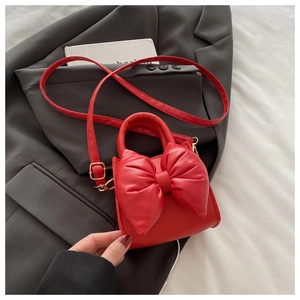 Detail of red crossbody bag featuring a large soft bow and polished leather texture
