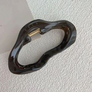 Close-up of brown irregular wavy hair claw clip showing glossy finish and metal spring