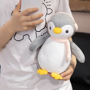 Plush penguin toy with pink earmuffs and scarf held by person for size reference