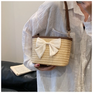Detail of hand-woven straw bucket bag featuring a large white chiffon bow and leather strap