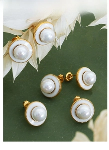 Close-up of pearl earrings with white enamel and gold beads on dark green backdrop