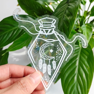 Hand holding holographic suncatcher sticker with potion bottle and moon dreamcatcher design