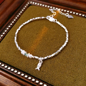 Detail of silver bead bracelet featuring white pearls and a small fish pendant