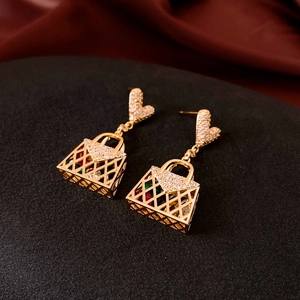 Macro shot of gold handbag earrings with crystal heart studs on luxury red silk background