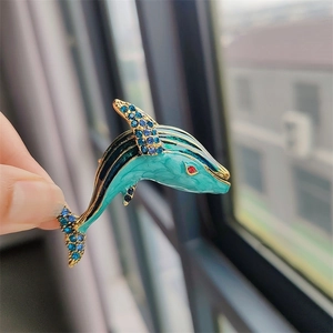 Detail of teal enamel dolphin brooch with blue rhinestones and gold metal edges