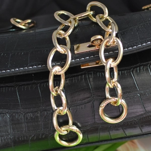 Bolso negro con textura de cocodrilo, cadena de aluminio dorada y cierre giratorio