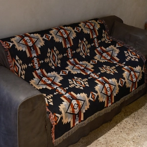 Detail of bohemian geometric woven blanket with tassels on a dark leather sofa
