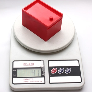 Dettaglio di una scatola scherzo rossa pesata su bilancia digitale che indica 41g