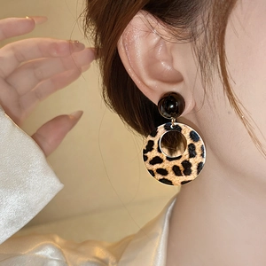 Close-up of leopard print acrylic hoop earrings with black round studs on female model