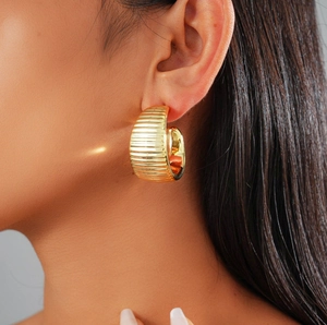 Polished golden C-shape stud earrings with textured stripes on female model