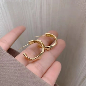 Pair of gold geometric C-shaped earrings held by hand to show size and metallic texture