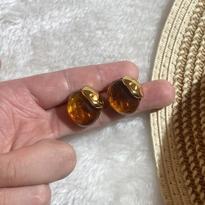 Elegant amber resin oval stud earrings with gold stainless steel edges held in hand