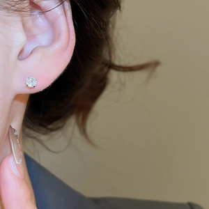 Macro shot of a U-shaped silver stud earring with a sparkling zircon on the earlobe