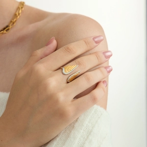 Detail of two-tone stainless steel wing ring worn on finger with gold chain background