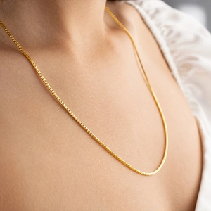 Detailed close-up of a 1.2mm gold box chain necklace worn on the neck for styling