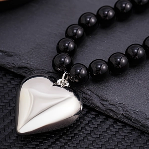 Close-up of a polished silver heart pendant on a black beaded necklace for men