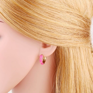 Close-up of pink enamel huggie hoop earring worn by a model with golden hair