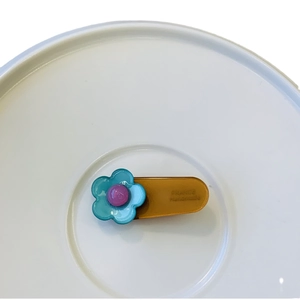 Sky blue flower hair clip with purple center and amber base on a white ceramic plate