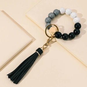 Boho wood bead keychain bracelet with black tassel and golden ring on beige surface