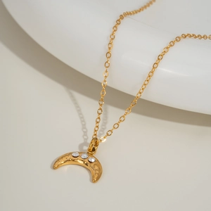 Detail of gold crescent moon necklace with clear crystals on a white ceramic plate