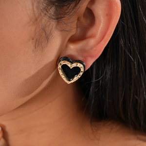 Close-up of heart-shaped earring featuring hammered gold frame and black inlay on model