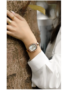 Close-up of a vintage oval gold watch with brown leather strap worn on a woman's wrist