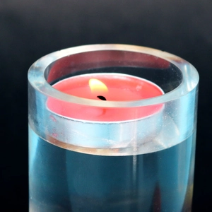 Macro shot of a cylindrical resin candle holder with a burning pink tea light candle