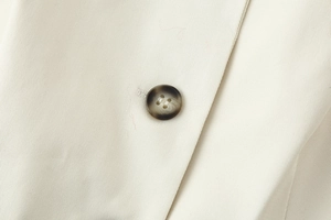 Close-up of amber marble button on beige woven vest fabric with fine twill texture detail