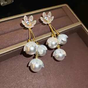 Boucles d'oreilles fleurs dorées avec perles blanches sur un plateau à bijoux en velours