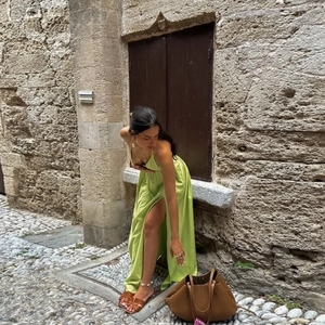 Detail of a grass green silk maxi dress paired with brown leather flat sandals on a stone street