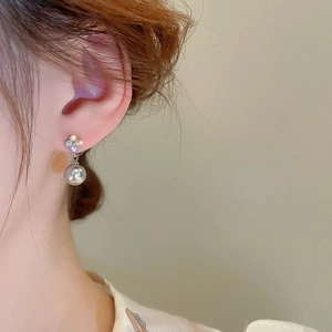 Macro detail of clover-shaped stud with inlaid zircons and a dangling lustrous pearl