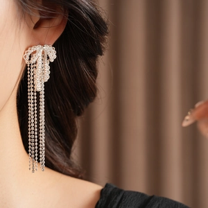 Close-up of silver bow earrings with sparkling tassel chains worn by a model