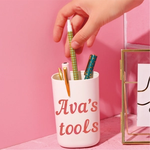 Close-up of a white pencil holder with Ava's tools text against a pink studio background