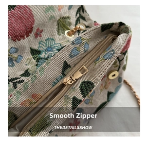 Detail view of smooth metal zipper and floral strawberry embroidery on a handbag