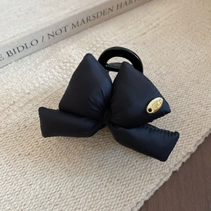 Detail of a black satin bow hair claw clip with a small gold metal logo on beige fabric