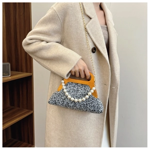 Detail of grey tweed evening bag featuring wooden frame handle and elegant pearl charm