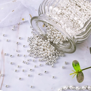 Macro shot of silver hollow metal beads scattered on a white marble surface for DIY jewelry