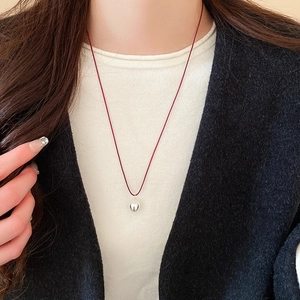 Detail view of heart-shaped silver pendant with vibrant red cord necklace on a model