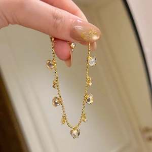 Close-up of golden heart bracelet with sparkling crystals and star charms on model's wrist