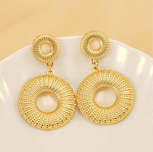 Detailed view of gold stainless steel earrings with woven texture on a ceramic plate