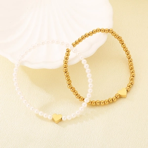 Close-up of heart charm on pearl and gold bead bracelets with white shell decoration