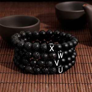 Detail of beaded bracelets featuring black lava stones and stainless steel letter charms