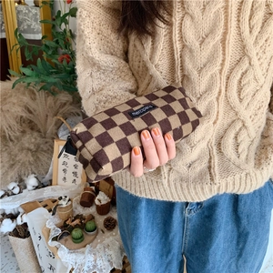 Close-up of a brown and beige checkered knit pencil case held by a person in a vintage setting