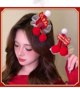 Close-up of red festive hair clip with plush pom poms and golden holiday embroidery