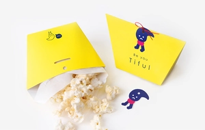 Detail of yellow candy gift box with Uare logo, red ribbon tie, and cartoon sticker