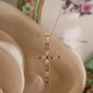 Gold plated cross necklace with colorful zircons and pearls on a silk background