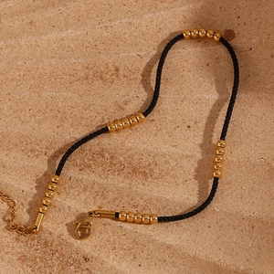 Detail of black string anklet with gold beads and lobster clasp on sandy texture