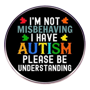 Round Autism awareness pin badge with colorful puzzle pieces on black metal background